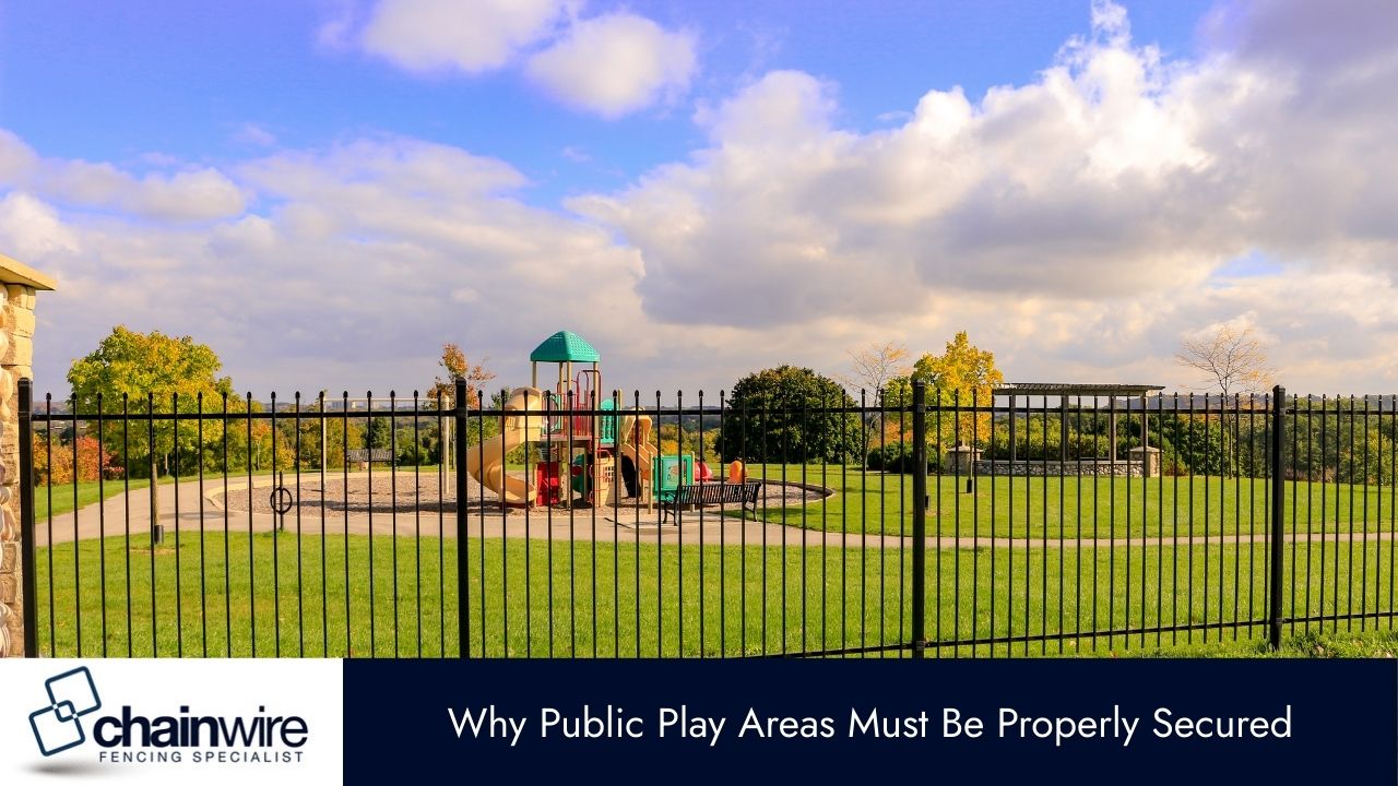 A public playground with a large grassy field and a colorful play structure is secured by a black metal fence in the foreground.