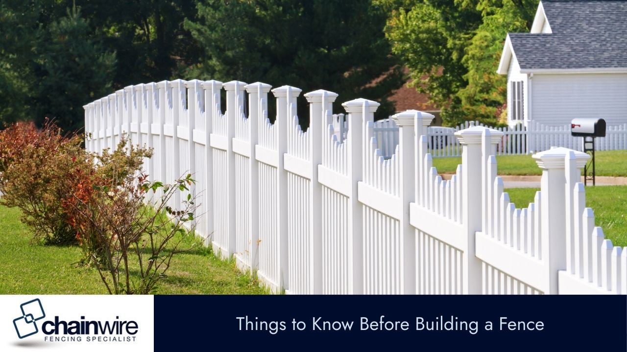 A long, curved white picket fence runs along a green lawn in front of a white house.
