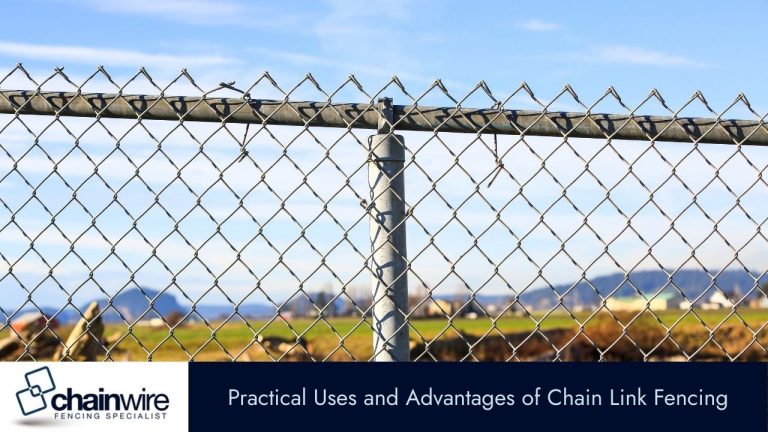 A close-up of a chain-link fence with a top rail, set against a backdrop of green fields and distant mountains.