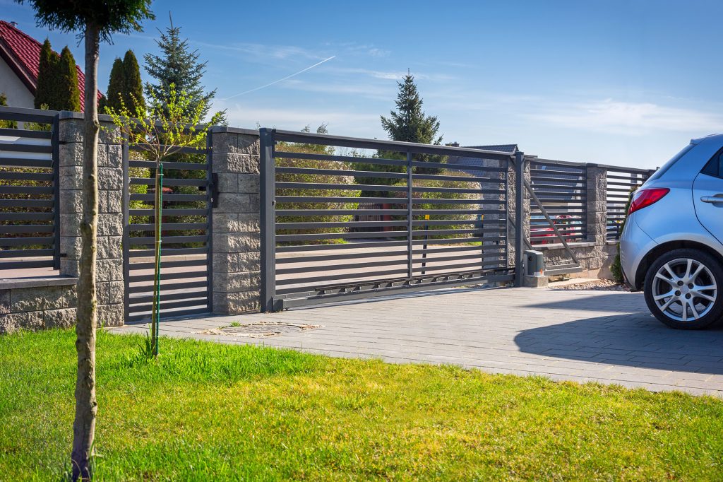 A wide shot of a modern residential driveway with a grey horizontal slat fence and an automatic gate.