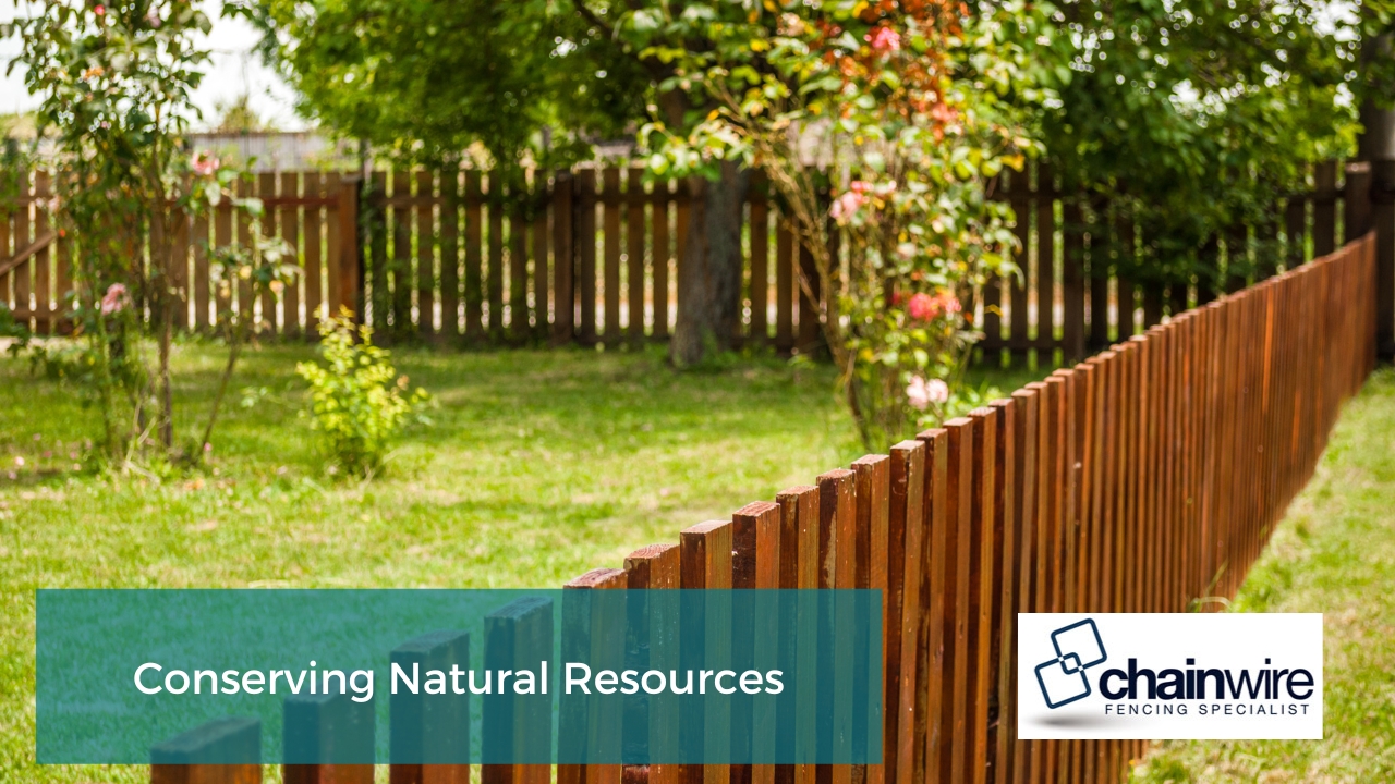 Wooden fence surrounding a green backyard with trees and flowering plants.