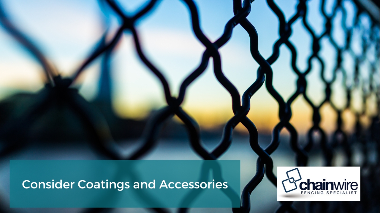 close-up of a chain link fence against a blurry background of a sunset. The fence is made of black metal wire that is in a diamond pattern