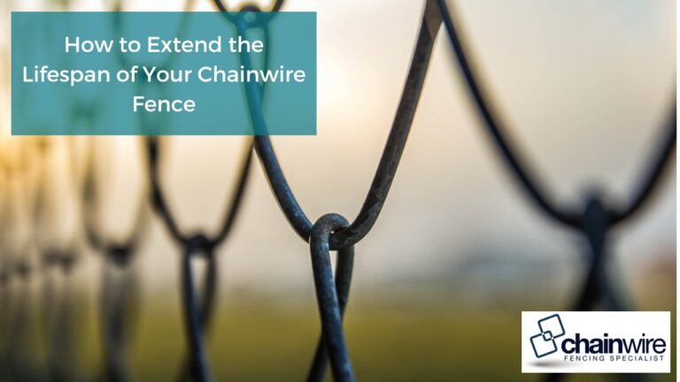 close-up of a chain link fence with a focus on the interweaving of the wires. The background is blurry, suggesting a field or outdoor setting. The wires are dark in color, possibly black or dark gray.