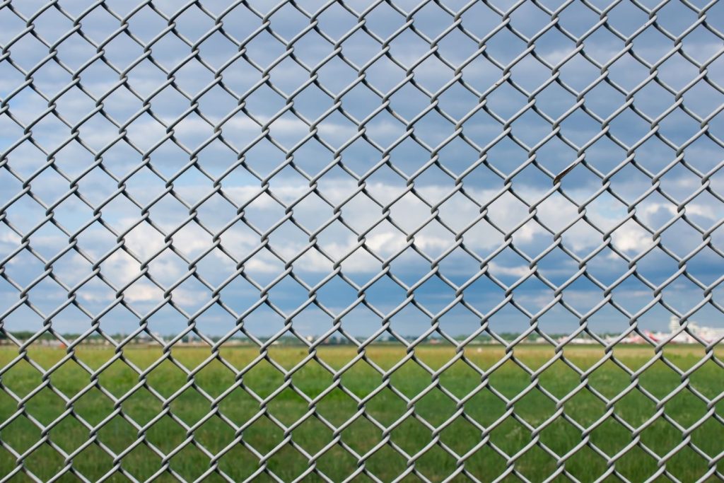 A wide view through a grey chain-link fence, which is in focus in the foreground.