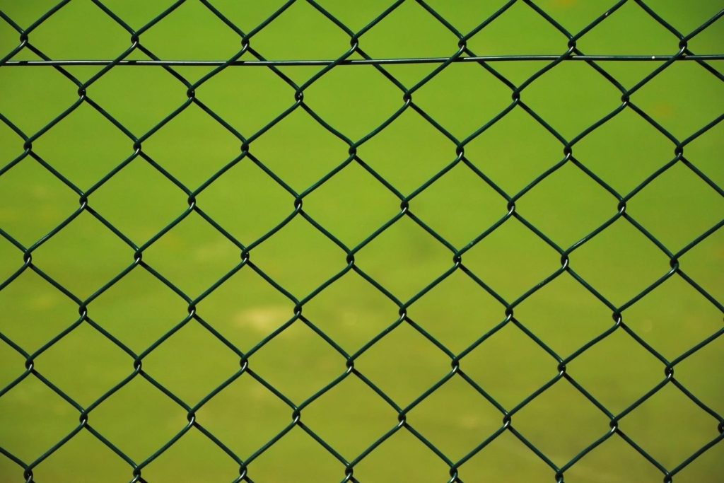 A close-up, head-on shot of a dark green chain-link fence, with the diamond-shaped mesh pattern clearly visible.