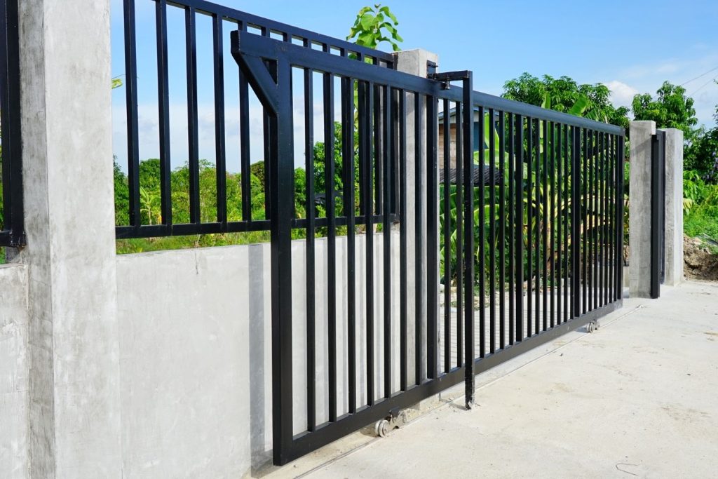 A newly installed black metal sliding gate, made of vertical bars, is partially open.